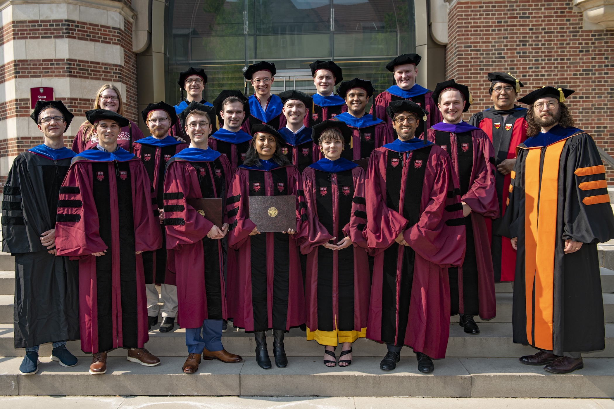 A group of 2025 Economics PhD graduates in full academic regalia in front of Saieh Hall