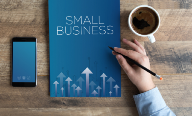 Hand holding pen above notebook that says "Small business"