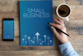 Hand holding pen above notebook that says "Small business"